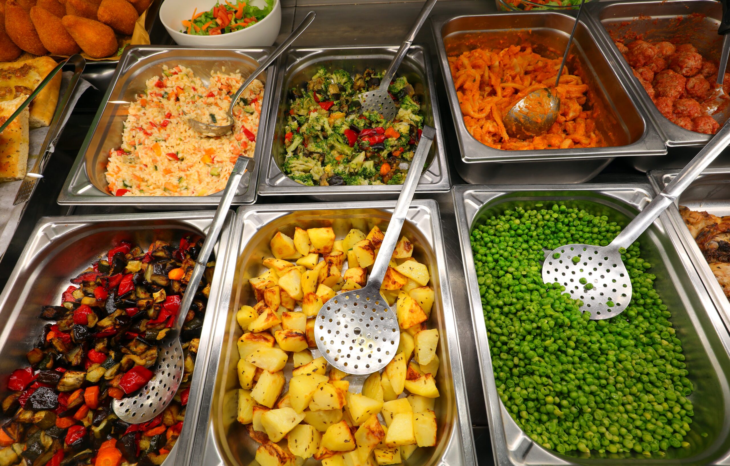 Many steel trays with vegetables and first courses in the self-service restaurant ideal for lunch break in the company or school canteen